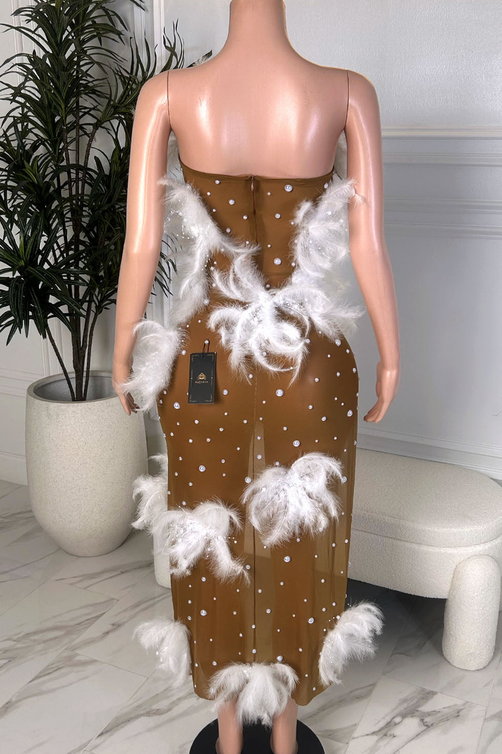 Nude illusion mesh maxi dress with white feather trim and pearl embellishments on mannequin, back view