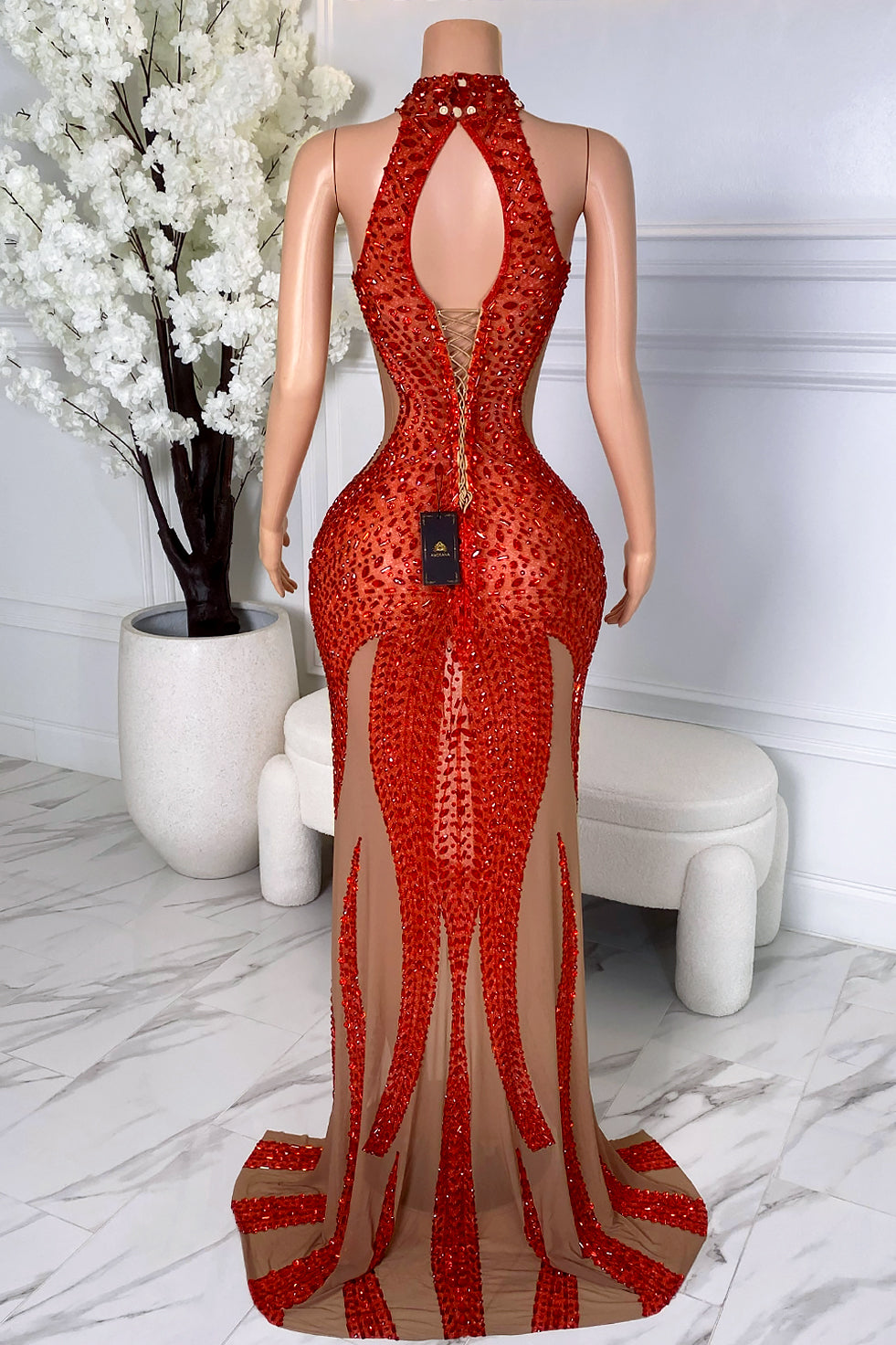 Back view of a red crystal illusion dress without cape showing an open back, lace-up detail, nude mesh panels, beaded design, and floor-length silhouette.