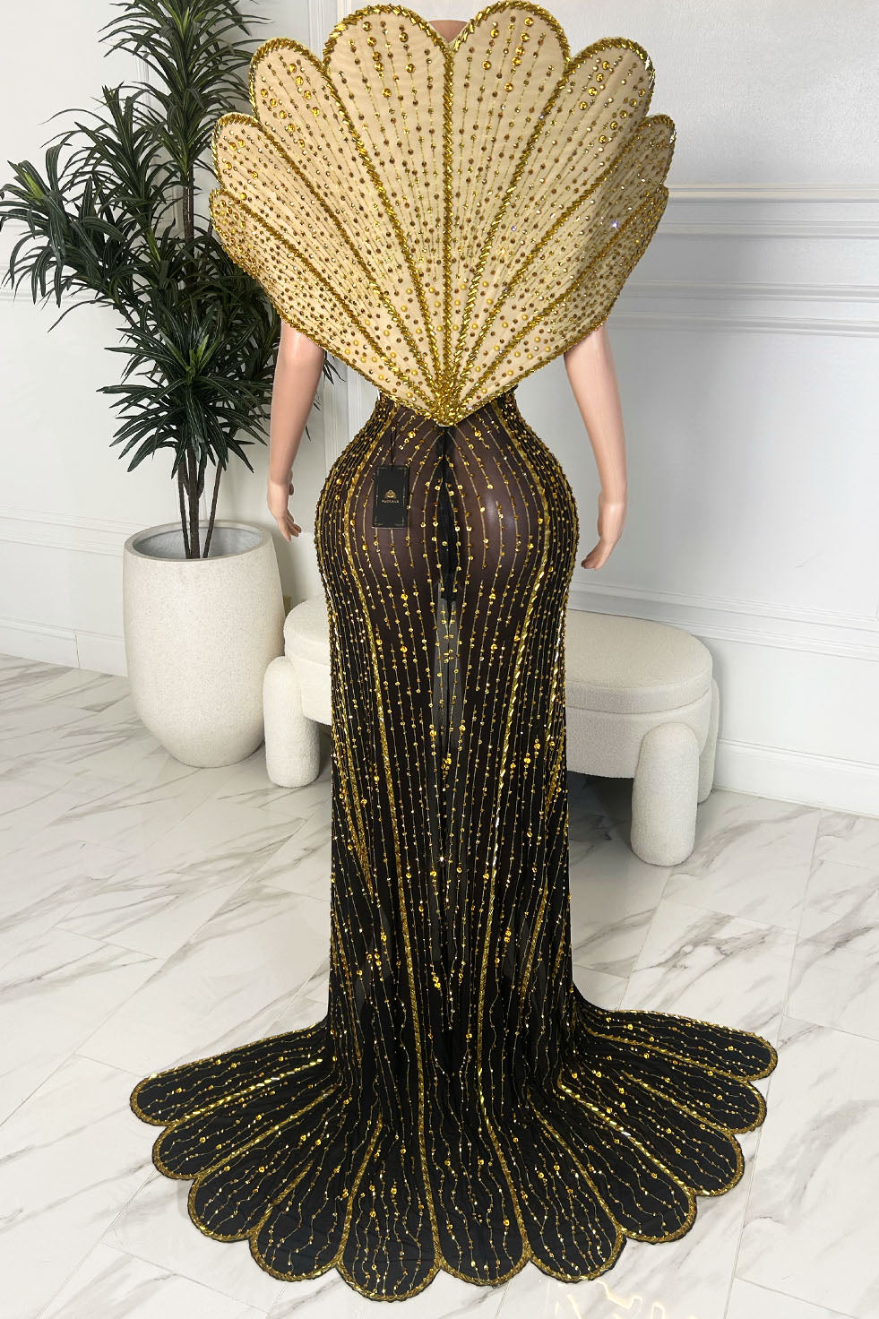 Back view of a black and gold embellished couture gown with oversized shell inspired back detail and scalloped train