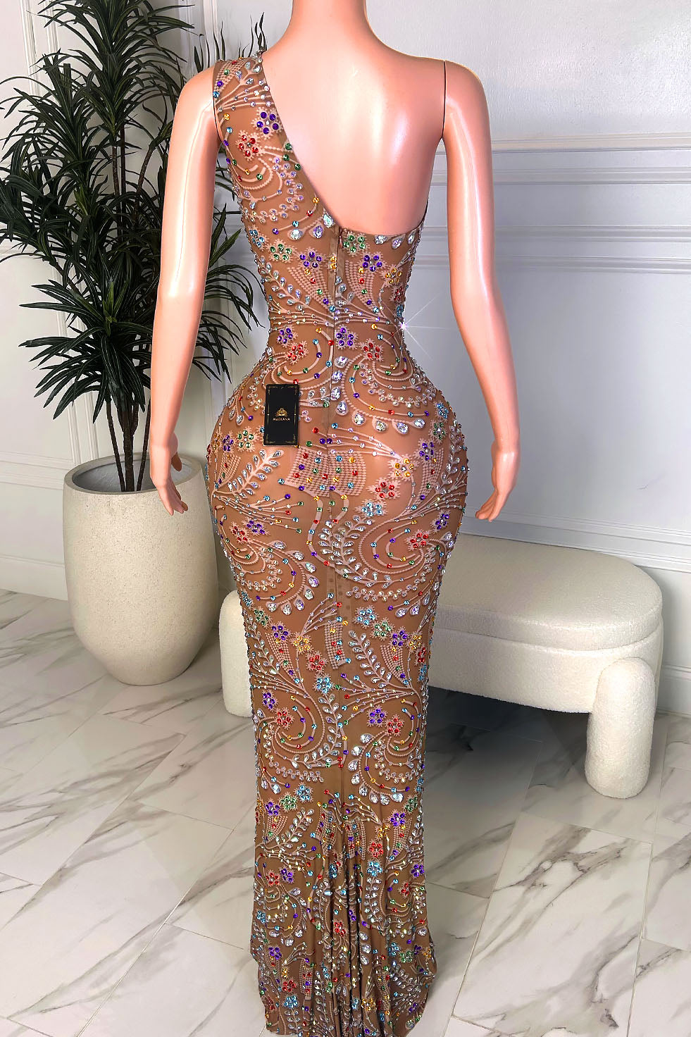 Back view of a one shoulder nude illusion gown with multicolor crystal embellishments, open back detail, and back zipper closure