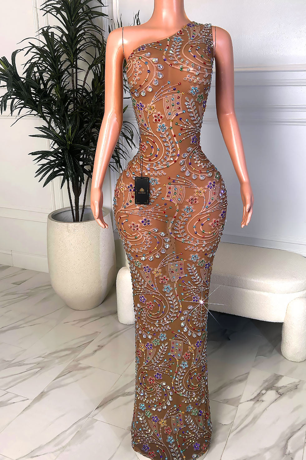 Front view of a one shoulder nude illusion gown with multicolor crystal embellishments and a fitted floor-length silhouette