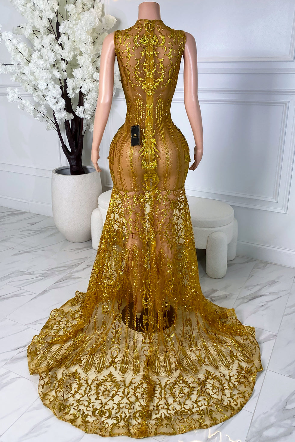 Back view of a gold lace train dress with sheer illusion detail, center zipper closure, fitted silhouette, ornate embellishments, and dramatic train.