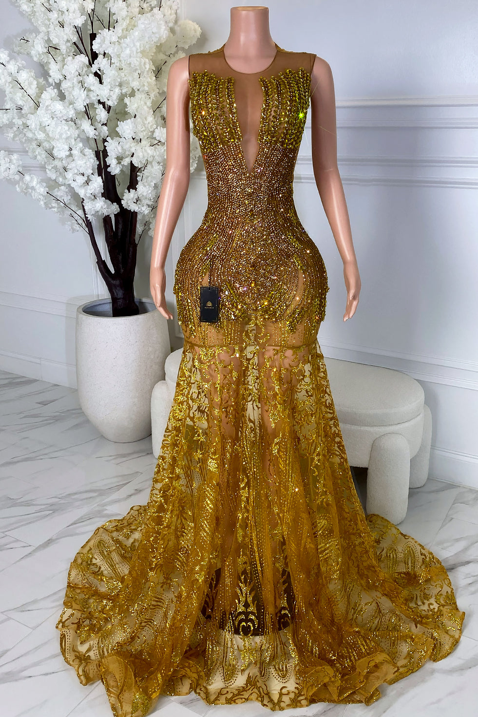 Wide front view of a gold crystal lace train dress with deep plunge neckline, sheer illusion base, fitted mermaid silhouette, and dramatic train