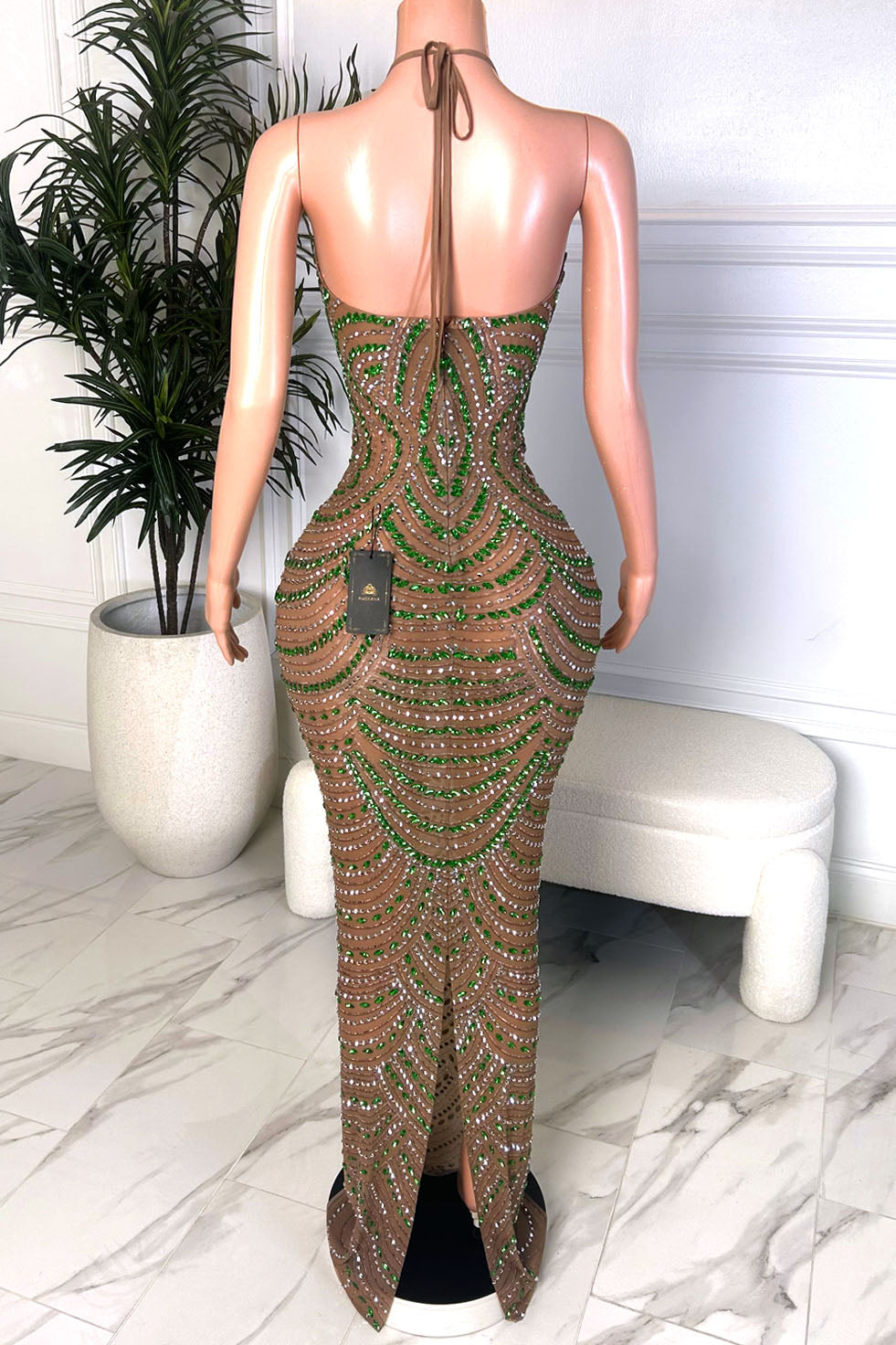 Back view of a nude illusion green crystal gown with a halter tie neckline, open back, and back slit detail
