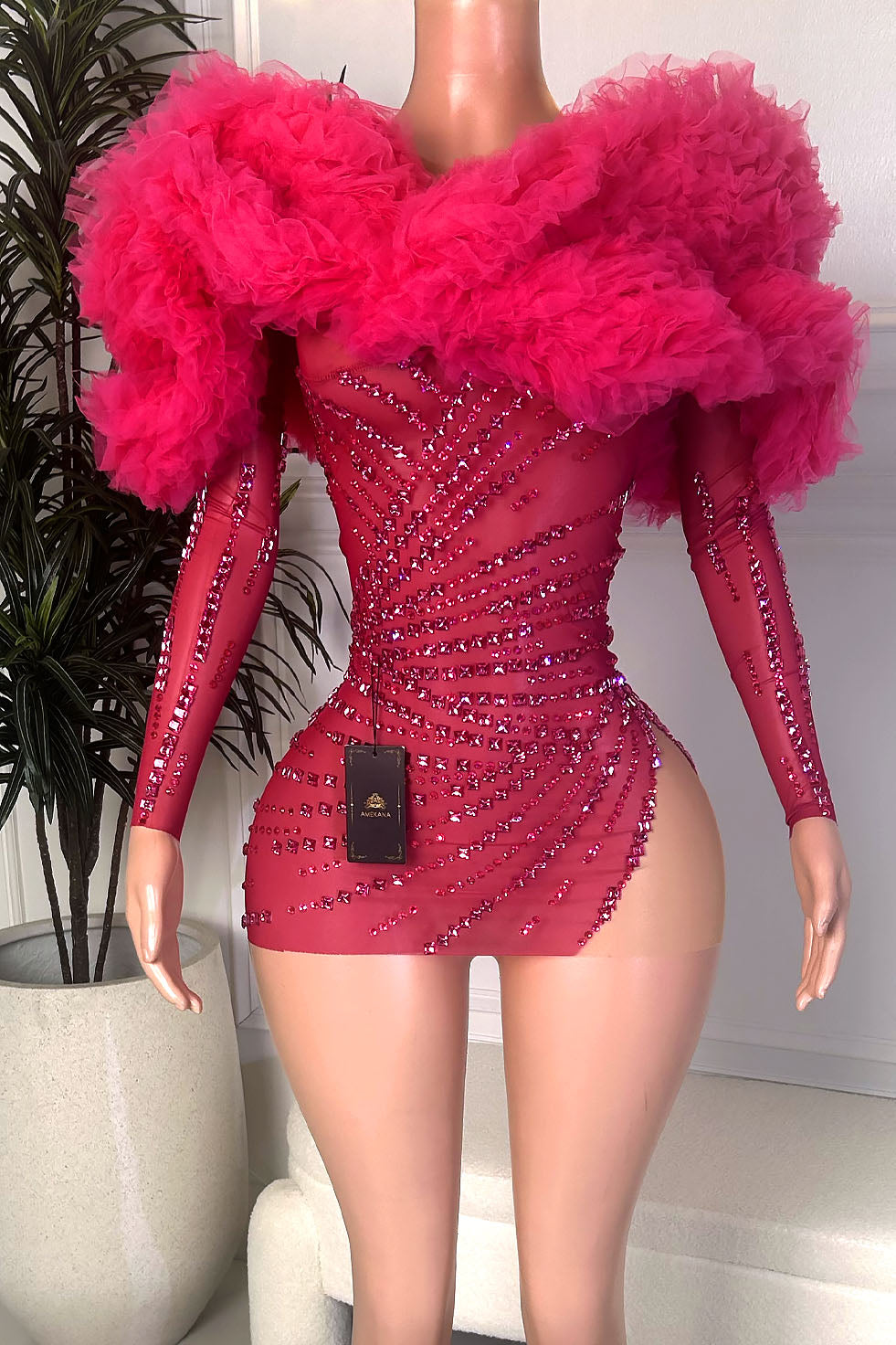 Front view of a hot pink rhinestone embellished mini dress with oversized tulle shoulder ruffles, sheer long sleeves, and fitted silhouette