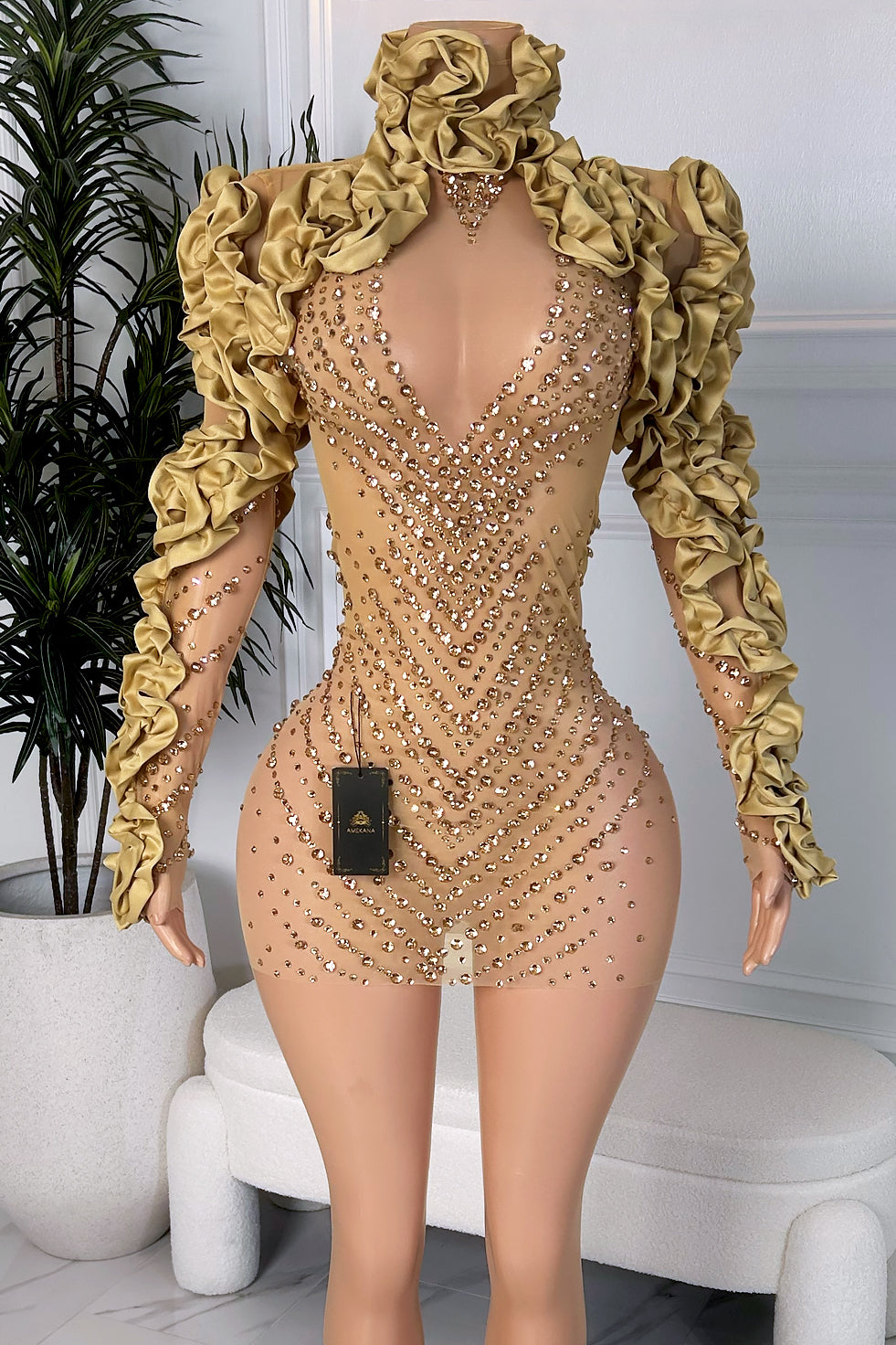 Front view of a champagne gold sheer mini dress with dense rhinestone embellishment, high neckline, and dramatic ruffle sleeves on a mannequin
