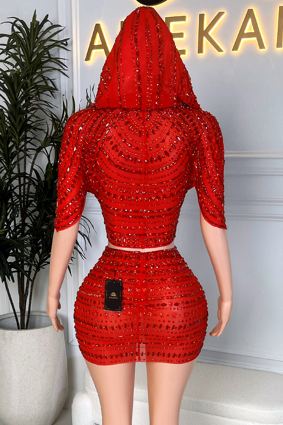 Red Hooded Skirt Set on mannequin, fully embellished red rhinestone hood and mini skirt, back view displaying curve hugging fit at Amekana showroom.