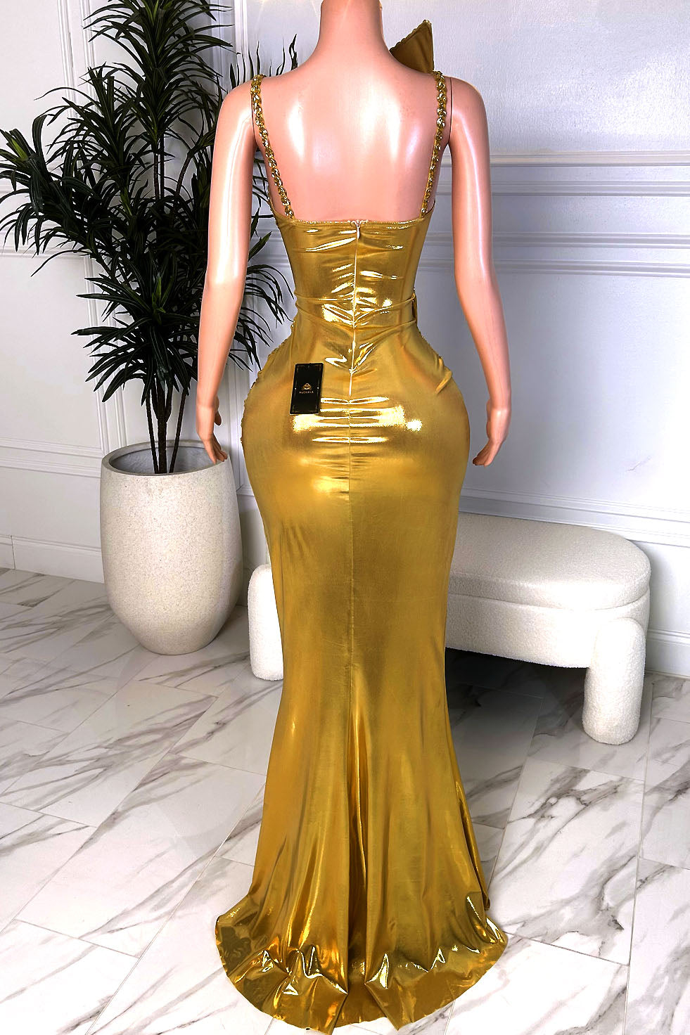 Back view of a metallic gold fitted evening gown with embellished straps, back zipper closure, and flared floor-length hem
