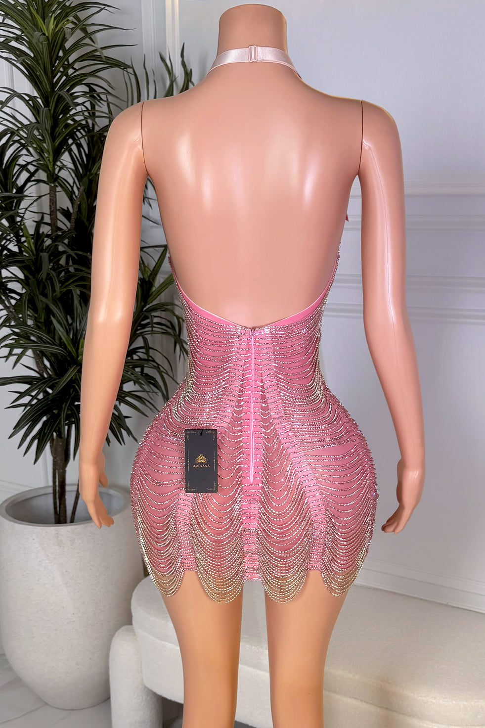 Back view of a pink crystal halter mini dress with low open back, adjustable neck strap, center zipper closure, rhinestone wave detailing, and scalloped hem.