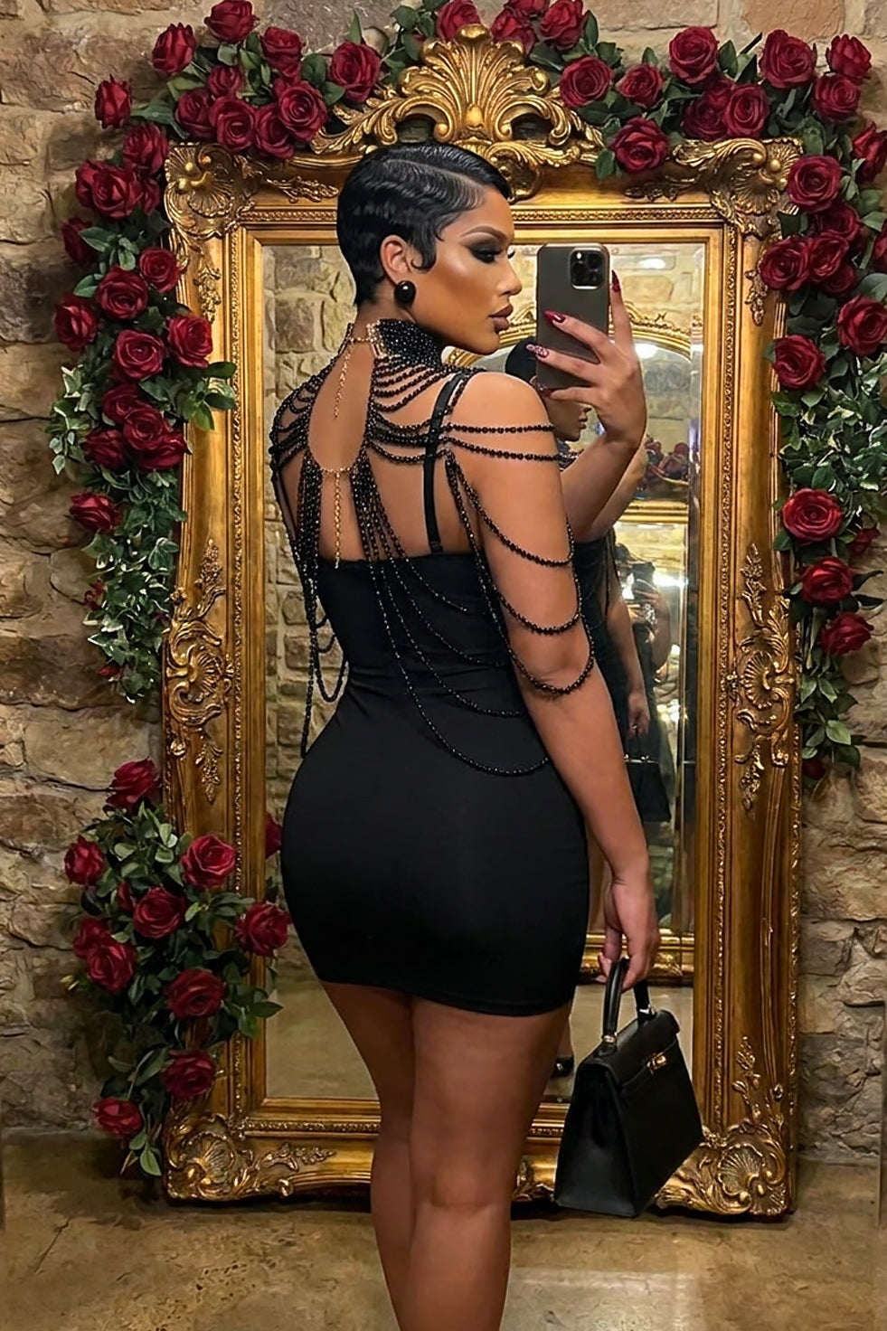 Back view of a black beaded shoulder drape accessory with a high collar, layered bead chains, and cape-inspired design styled over a black dress.