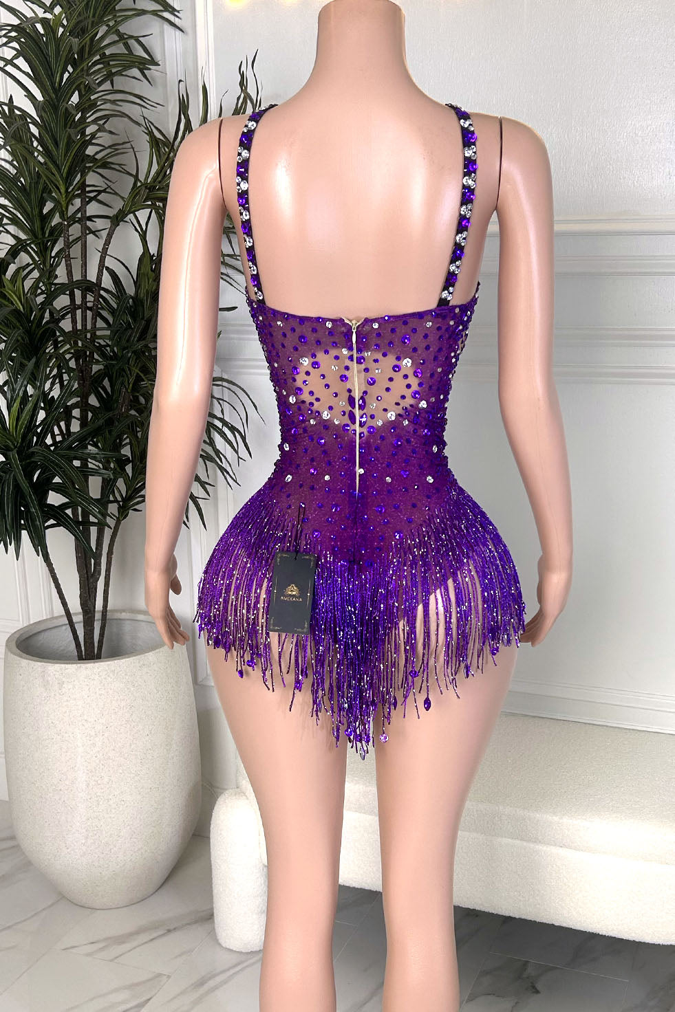 Back view of a purple rhinestone fringe illusion mini dress with embellished straps, a sheer nude illusion back, silver crystal accents, and beaded fringe detailing