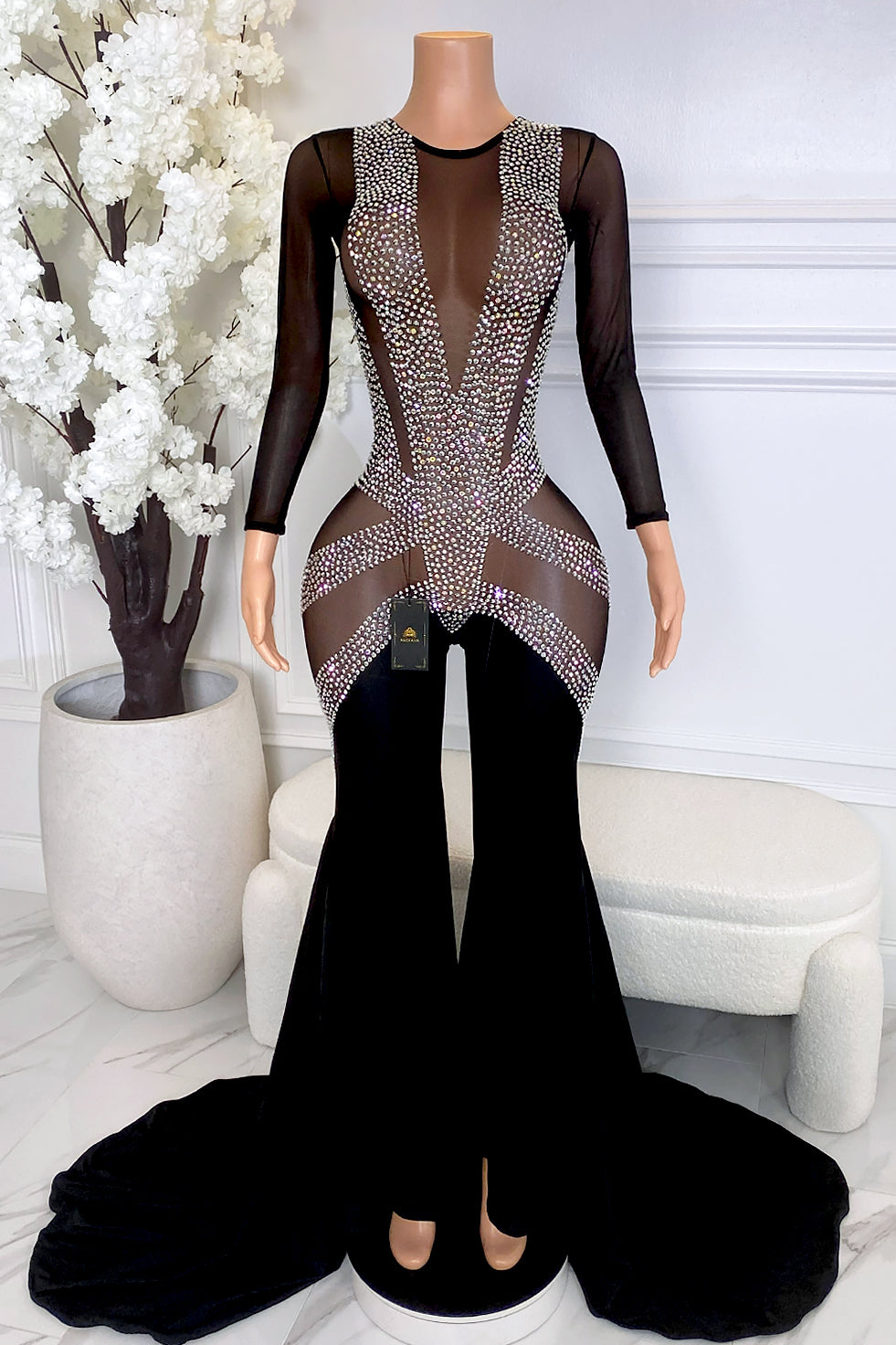 Front view of Sazzy Black Rhinestone Mesh Jumpsuit featuring sheer black mesh, silver rhinestones, long sleeves, fitted illusion bodice, flared legs, and dramatic floor-length train