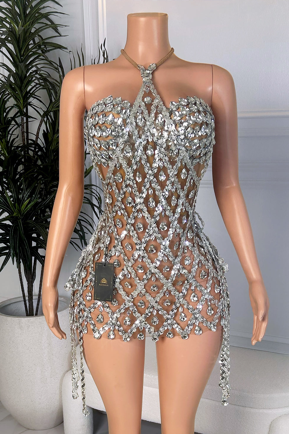 Back view of a silver crystal halter mini dress with sheer illusion detailing and teardrop crystal embellishment on a mannequin