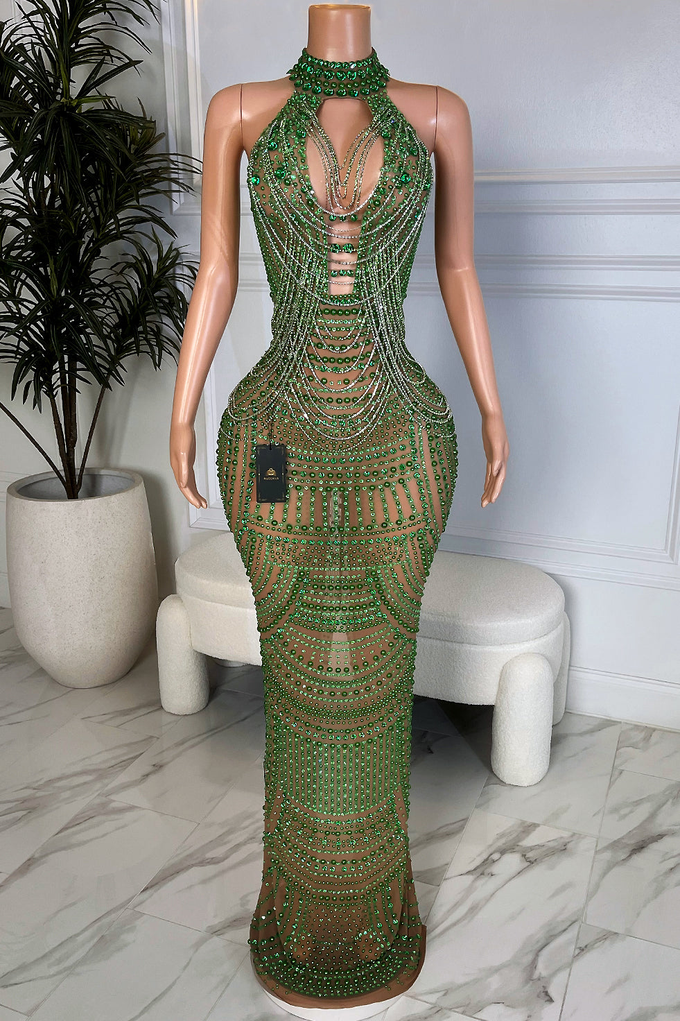 Back view of So Mysterious Maxi, a nude mesh maxi dress covered in emerald green rhinestones with a halter neckline and back slit.