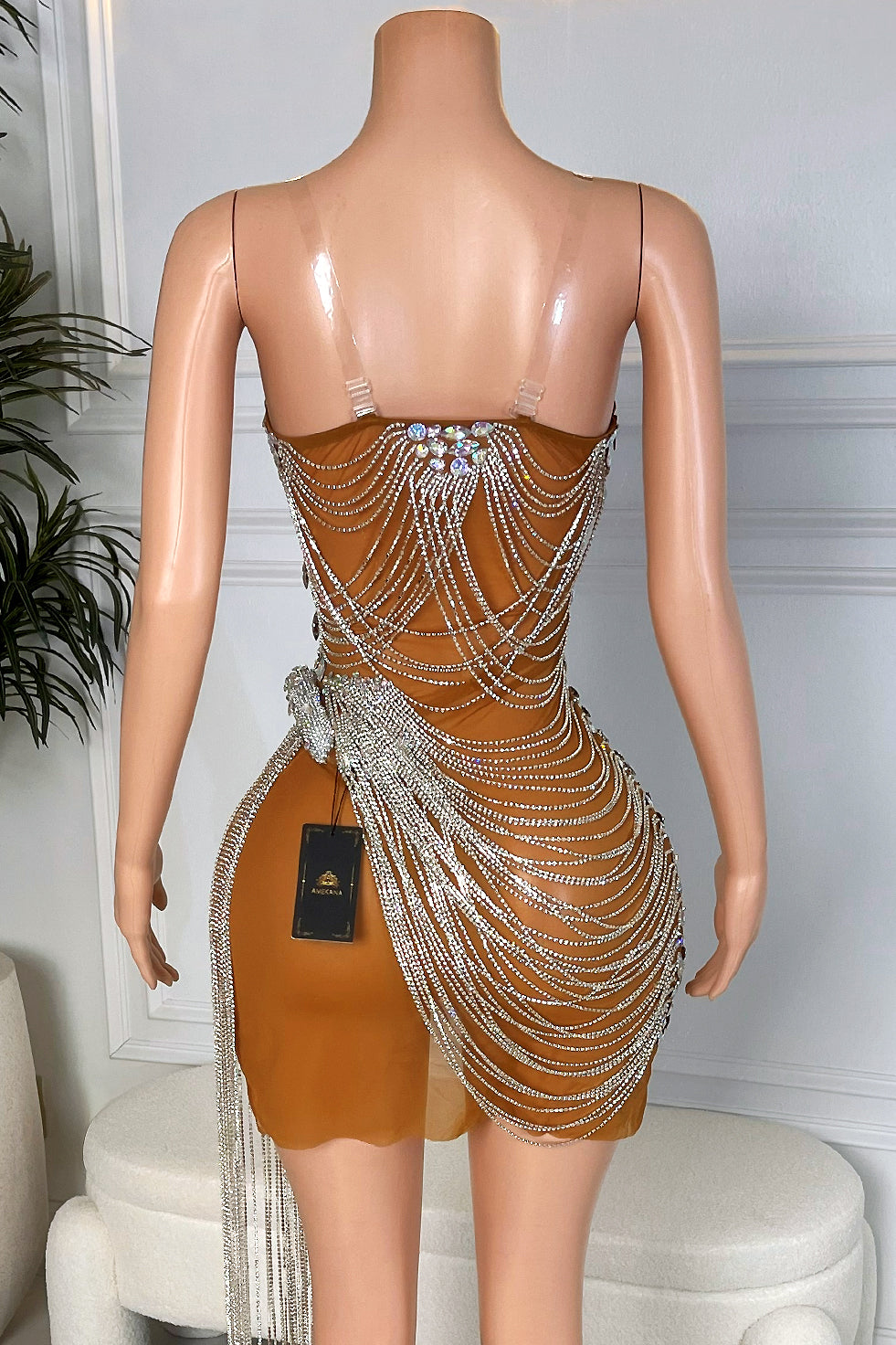 Back view of a nude brown rhinestone chain mini dress with clear straps and cascading silver crystal chains over the hips