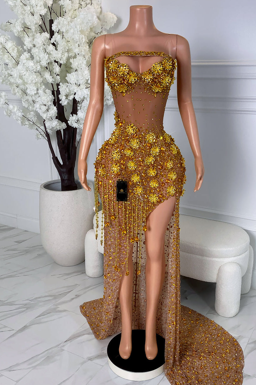 Front view of a nude illusion gold floral crystal dress with strapless neckline, high slit, gold appliqué details, bead accents, and flowing train.