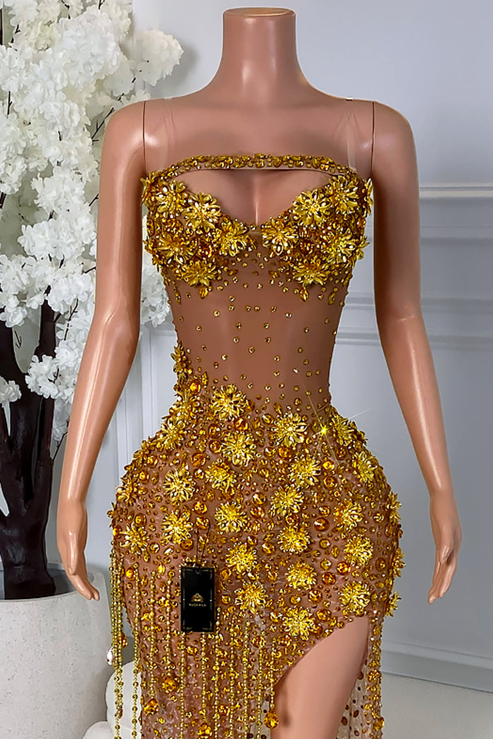Close-up view of a gold floral crystal dress showing the structured bust, sheer illusion bodice, gold appliqué flowers, and sparkling bead embellishments