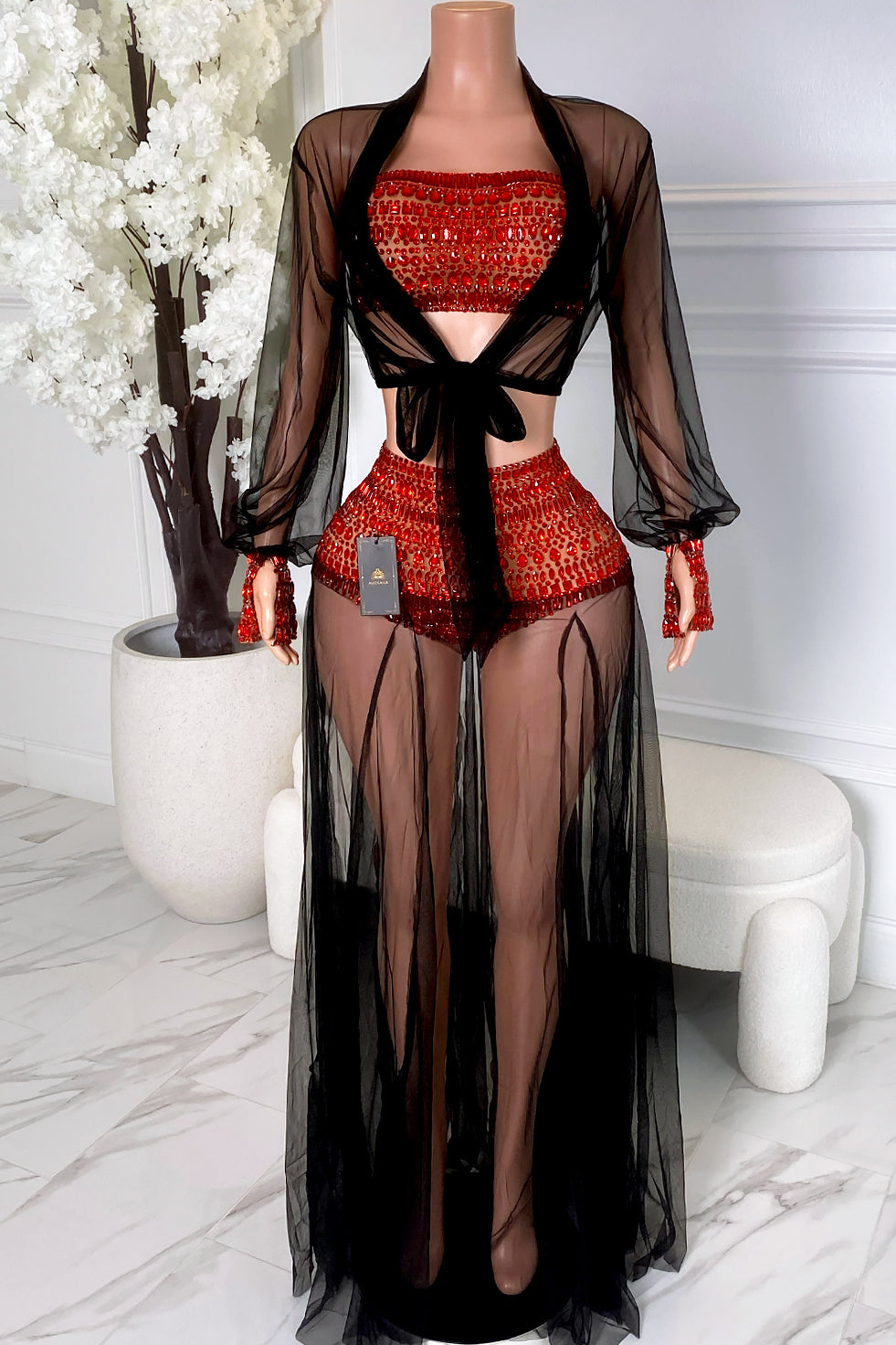 Front view of a red crystal black mesh skirt set with bandeau top, matching mini skirt, sheer long sleeve cover-up, front tie detail, and flowing maxi overlay.